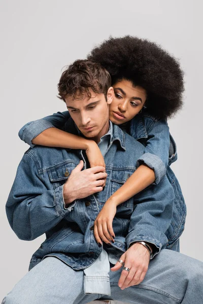 Brunette african american woman leaning on young man in denim outfit isolated on grey — Fotografia de Stock