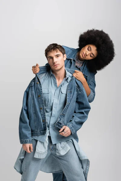 Curly african american woman adjusting denim jacket of man isolated on grey — Stock Photo