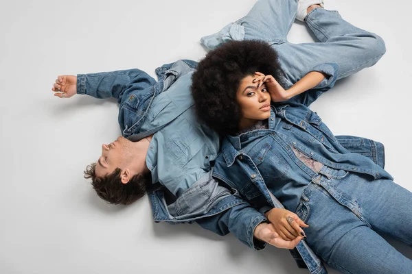 Top view of stylish african american woman in denim clothes lying with man on grey background — Stock Photo