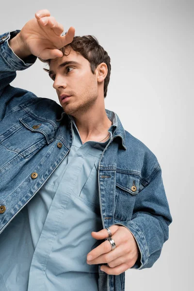 Jovem elegante em roupas jeans posando e olhando para longe isolado em cinza — Fotografia de Stock