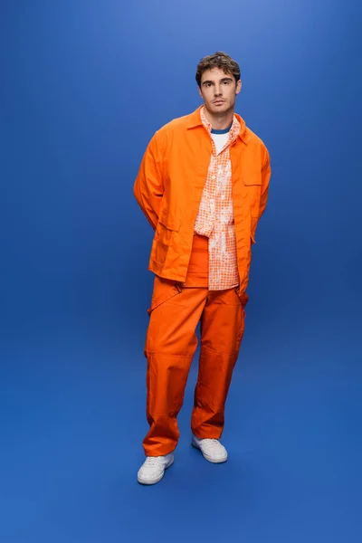 Full length of man in bright overall and jacket standing on blue background — Stock Photo