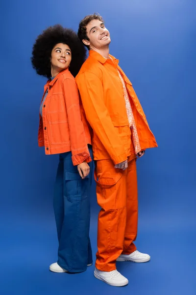 Усміхнені міжрасові моделі в помаранчевих куртках, що стоять назад на синьому фоні — стокове фото