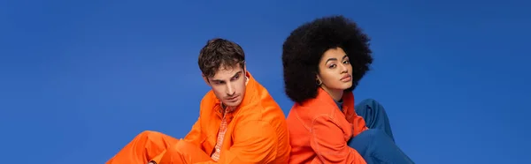 African american model looking at camera near man in orange clothes isolated on blue, banner — Photo de stock