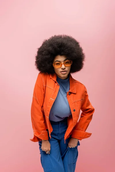 Mujer afroamericana en gafas de sol y traje brillante aislado en rosa — Stock Photo