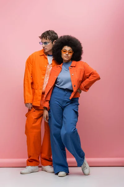 Femme afro-américaine élégante en lunettes de soleil posant près de l'homme sur fond rose — Photo de stock