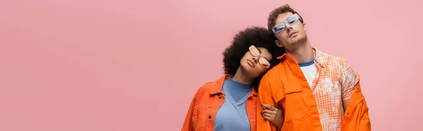Стильні багатоетнічні моделі в сонцезахисних окулярах, що стоять ізольовані на рожевому, банер — стокове фото