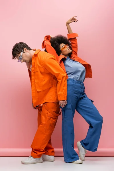 Full length of stylish multiethnic couple in sunglasses posing on pink background — Fotografia de Stock