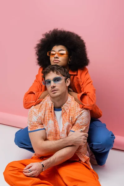 Stylish african american woman posing with young man in sunglasses on pink background — Stockfoto