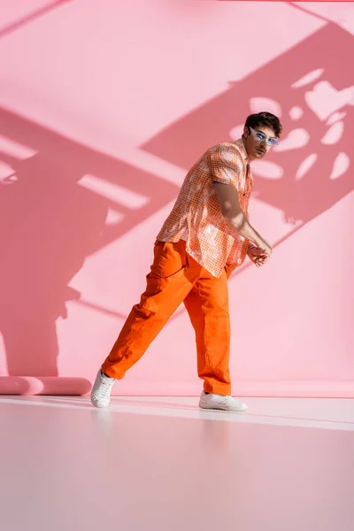Stylish brunette man in sunglasses looking at camera on pink background with shadow and light — Stock Photo