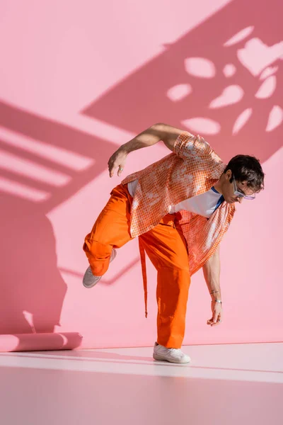 Homme élégant en lunettes de soleil et salopettes posant sur fond rose avec ombre — Photo de stock