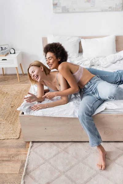 High angle view of young interracial women in jeans and lingerie having fun on bed at home — Stock Photo