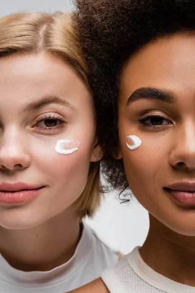 Nahaufnahme von jungen interrassischen Frauen mit Gesichtscremeabstrichen isoliert auf grau — Stockfoto