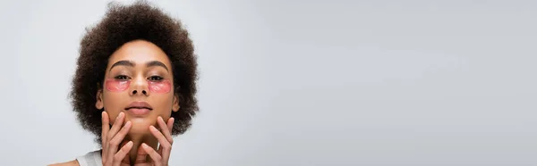 Retrato de mujer afroamericana morena con parches en los ojos tomados de las manos cerca de la cara aislada en gris, pancarta - foto de stock