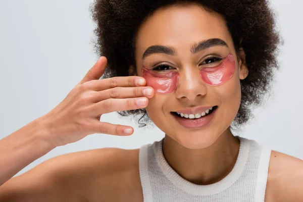 Happy african american model applying collagen eye patches while looking at camera isolated on grey — Stock Photo