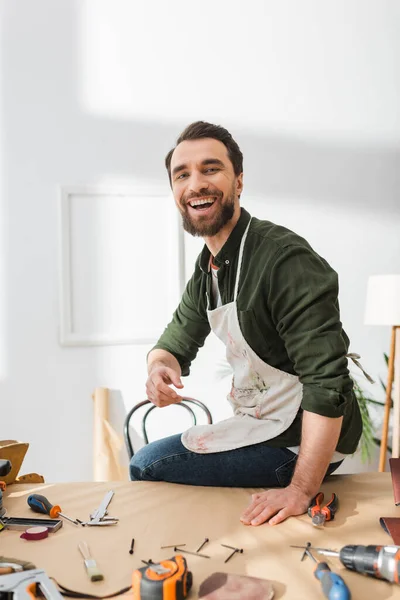 Smiling artisan in apron looking at camera near tools in workshop — Stock Photo