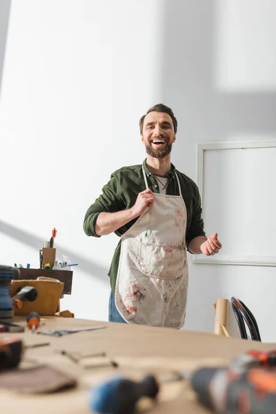 Positive craftsman in dirty apron standing in workshop — Stock Photo