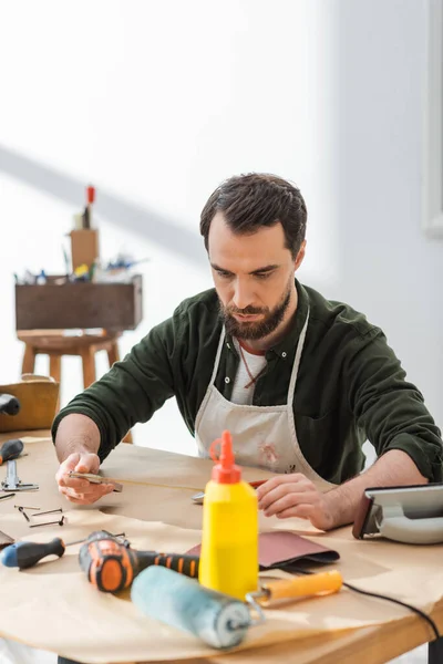 Artigiano in grembiule con attrezzo quadrato vicino alle attrezzature in officina — Foto stock