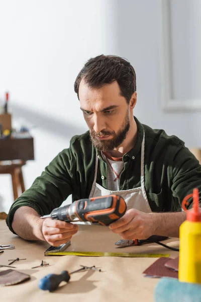 Artisan barbu dans le tablier tenant tournevis électrique dans l'atelier — Photo de stock