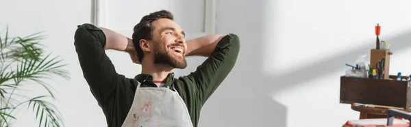 Positive carpenter in apron resting in workshop, banner — Stock Photo