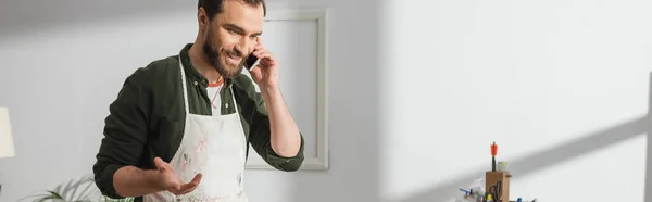 Lächelnder Tischler in Schürze, der in der Werkstatt mit dem Smartphone spricht, Banner — Stockfoto