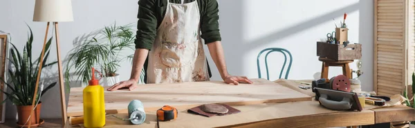 Cropped view of repairman in apron standing near wooden board and tools in workshop, banner — Photo de stock