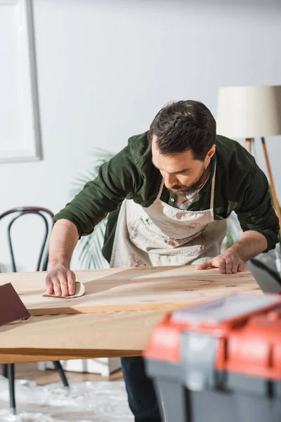 Craftsman in dirty apron sanding wooden board — Foto stock