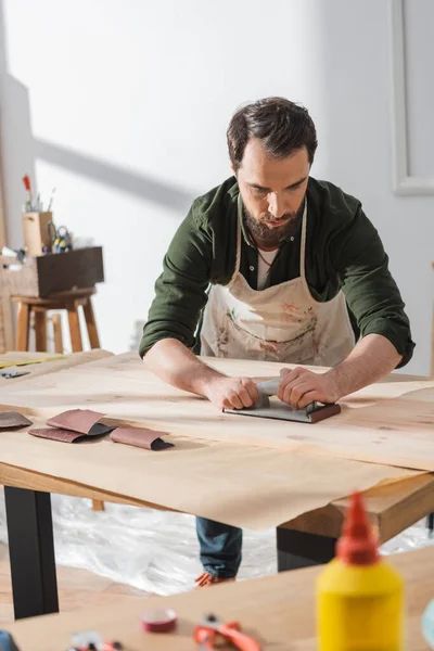 Craftsman sanding surface of wooden board in workshop - foto de stock