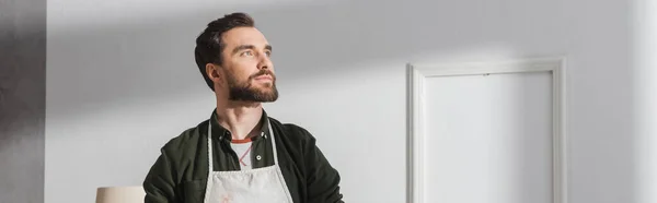Dreamy craftsman in apron looking away in workshop, banner — Stock Photo