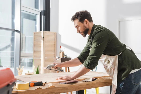 Side view of restorer working with sanding tool and surface of wooden board - foto de stock