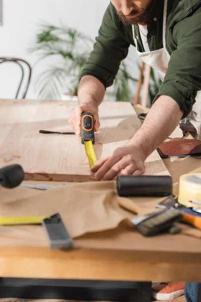Cropped view of bearded restorer measuring wooden board with ruler in workshop — Stock Photo
