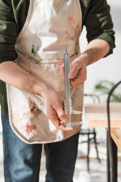 Cropped view of restorer in apron holding calipers in workshop — Stock Photo
