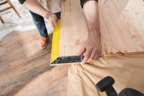 Vue recadrée du charpentier à l'aide d'un outil carré sur une planche en bois — Photo de stock