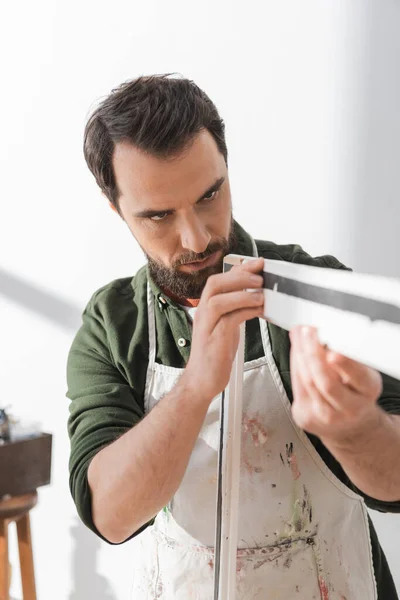 Focused restorer looking at wooden picture frame in workshop — Stock Photo