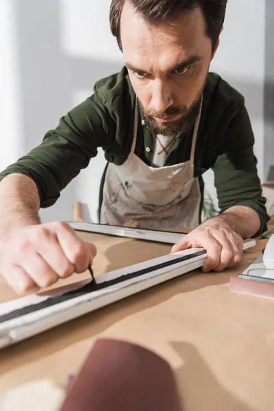 Bearded restorer in apron working with picture frame in workshop — Foto stock