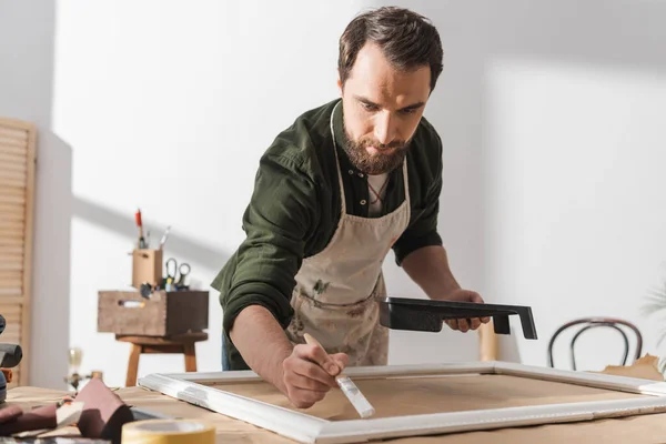 Restorer in apron painting on wooden picture frame on table in workshop — Stock Photo