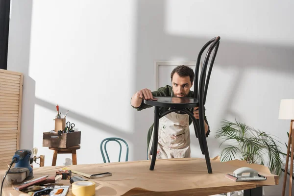Restorer in apron sanding wooden chair in workshop — Fotografia de Stock