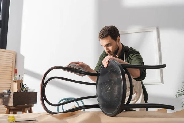 Artigiano levigatura vernice su sedia di legno vicino strumento quadrato in officina — Foto stock