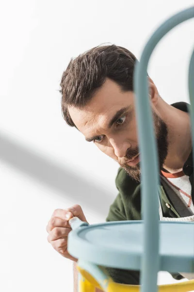 Bearded restorer repainting blurred chair in workshop — Stockfoto