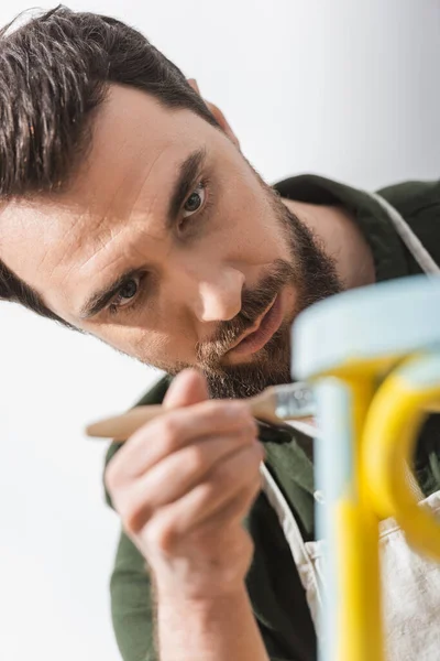 Focused repairman painting on blurred chair in workshop — Stock Photo