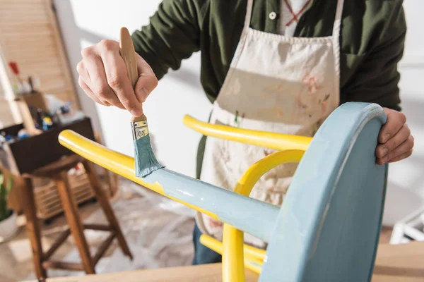 Cropped view of craftsman painting on wooden chair in blurred workshop — Foto stock