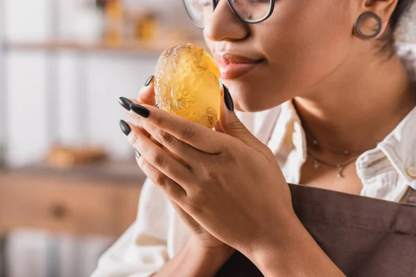 Cropped view of african american craftswoman enjoying scent of handmade soap in blurred workshop — Stock Photo