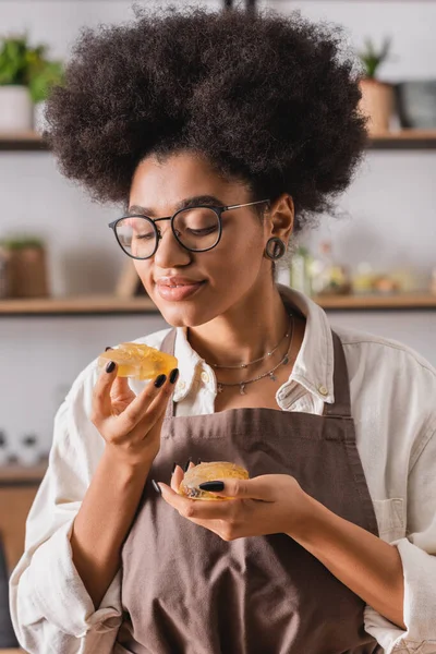 Задоволена афроамериканська жінка в окулярах і фартухах тримає бруси мила ручної роботи в майстерні ремесел — стокове фото