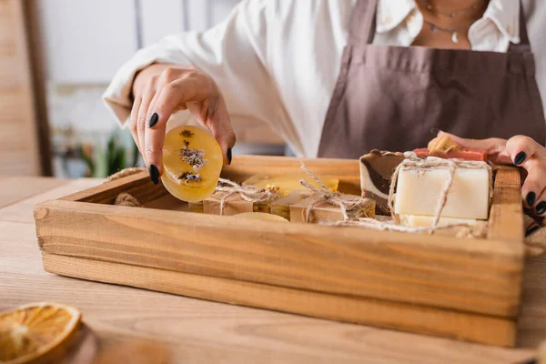 Partial view of african american craftswoman showing bar of herbal soap near wooden tray in workshop — Stock Photo