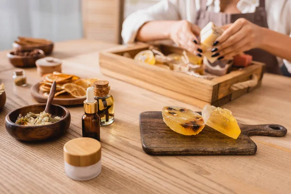 Tavolo in legno con sapone fatto a mano e ingredienti naturali vicino ritagliato artigiana afroamericana su sfondo sfocato — Foto stock