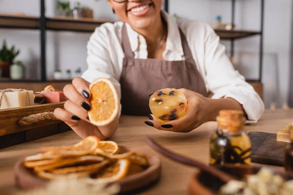 Cropped view of african american woman holding dried orange slice and homemade soap in craft workshop — Stock Photo