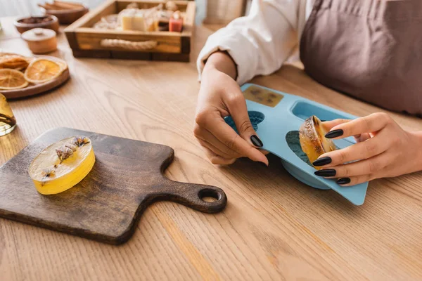Cropped view of african american woman taking soap bar off silicone mold near chopping board on wooden table - foto de stock