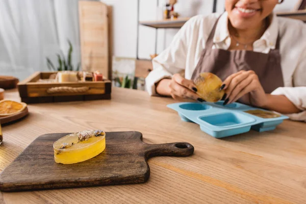 Selective focus of herbal soap on chopping near cropped african american woman and silicone mold on blurred background — Stock Photo