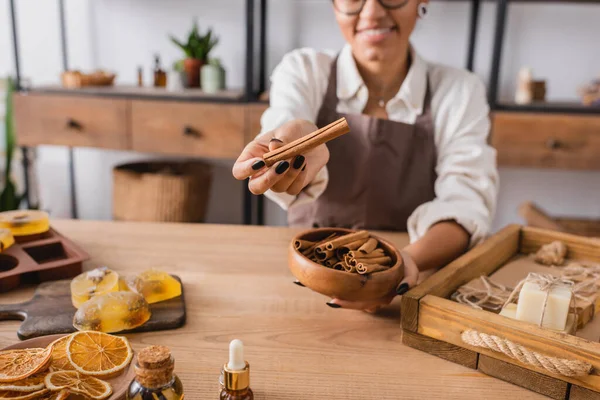 Cropped view of smiling african american woman holding cinnamon sticks near handmade soap and dried orange slices — Stock Photo