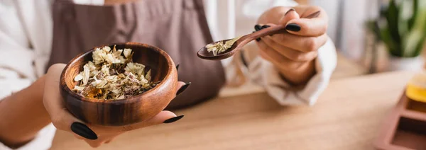 Cropped view of african american woman holding wooden bowl and spoon with dried herbs in craft workshop, banner — Stock Photo