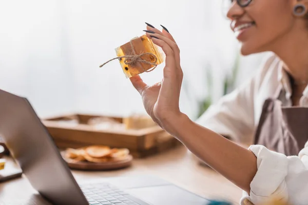 Cropped view of happy african american woman showing herbal soap during video call on laptop in craft workshop — Stock Photo